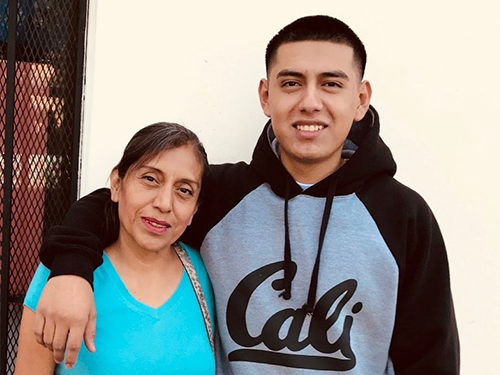 son wearing a black and gray sweater with his arm around his mother's shoulders