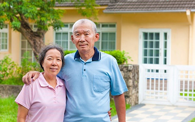 Asian couple standing in front of a yellow house